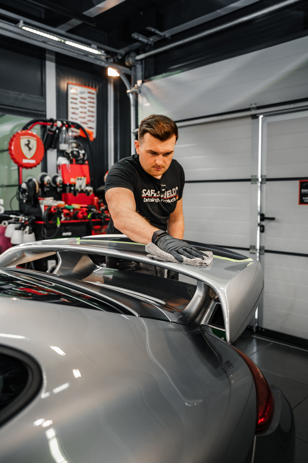 Tim removing residue from a sports car's rear spoiler with a grey 400 GSM microfibre cloth