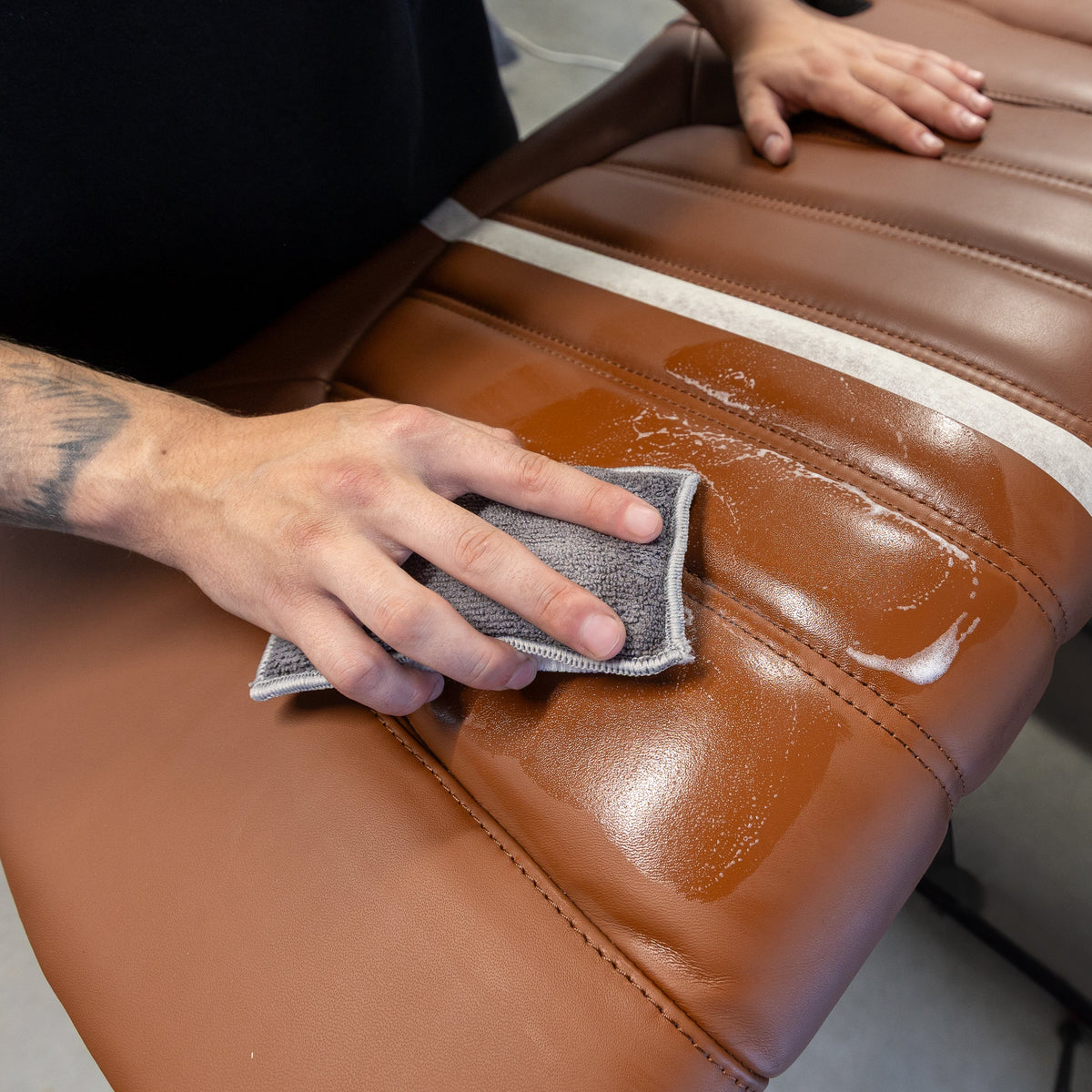 Cleaning a brown leather seat with a scrub pad